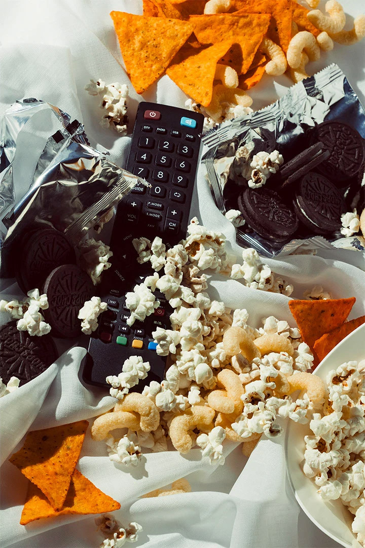 Photography of a messy desk with snacks and a TV remote